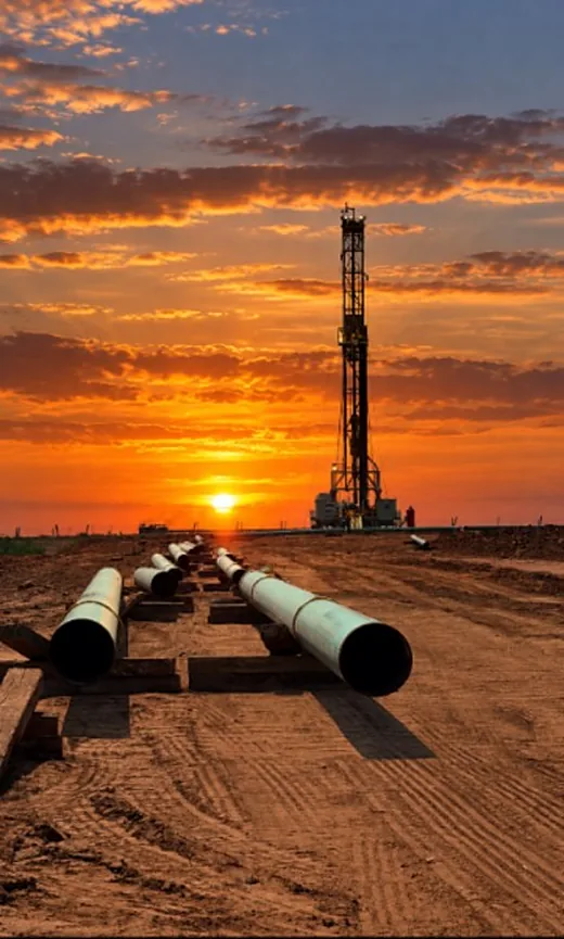 Pipe on skids in front of a rig at sunset